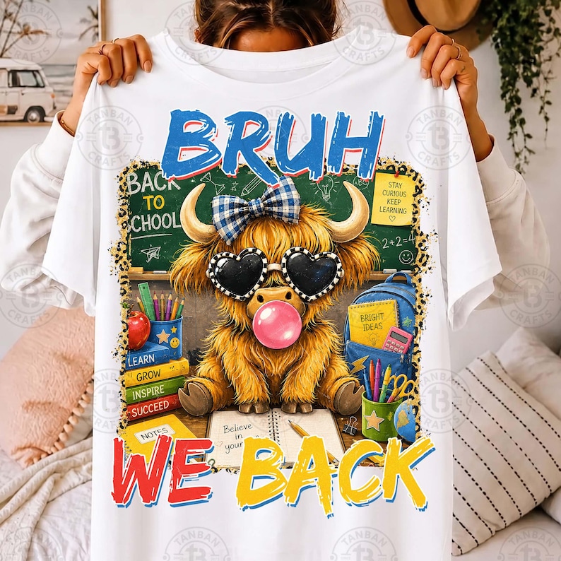 May include: A white t-shirt featuring a graphic of a fluffy Highland cow wearing a blue plaid bow and heart-shaped sunglasses while blowing a pink bubble. The cow sits before a chalkboard with the text BRUH WE BACK and school supplies.