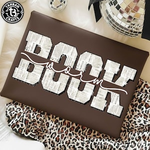May include: A brown rectangular pillow with the word "BOOM" in large, newspaper-print letters, and the word "WOW" in a white cursive font. The pillow is on a leopard print fabric.