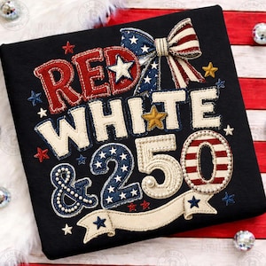 以下が含まれることがあります： 愛国的なデザインの黒いTシャツ。「RED WHITE & 250」の文字が赤、白、青で描かれ、星とリボンのアクセントが施されています。デザインは、下部にバナーが付いた刺繍です。