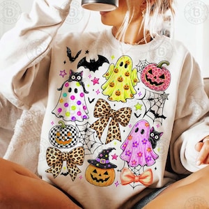May include: A cream-colored crewneck sweatshirt featuring a colorful Halloween-themed graphic print. The design includes ghosts, jack-o'-lanterns, leopard print bows, spiderwebs, bats, and stars in shades of pink, yellow, orange, and black.