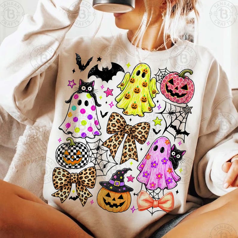 May include: A cream-colored crewneck sweatshirt featuring a colorful Halloween-themed graphic print. The design includes ghosts, jack-o'-lanterns, leopard print bows, spiderwebs, bats, and stars in shades of pink, yellow, orange, and black.