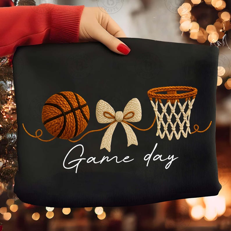 May include: Black decorative pillow featuring a basketball, a bow, and a basketball net design. The words "Game day" are written in white script. The basketball is brown and orange, and the net is beige.