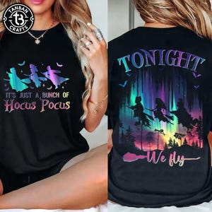 Puede incluir: Camiseta negra con un gr&aacute;fico colorido de brujas en escobas y el texto "It's Just a Bunch of Hocus Pocus" en la parte delantera. La parte trasera de la camiseta tiene el texto "Tonight We Fly".