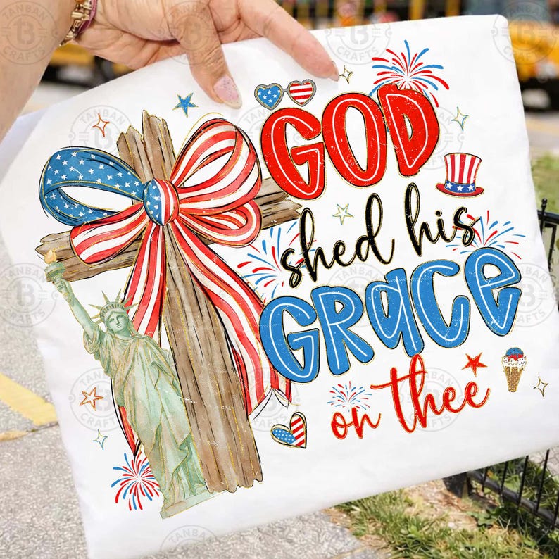 May include: White pillow with a patriotic design featuring a wooden cross adorned with a red, white, and blue bow. The Statue of Liberty is on the left. The text reads "GOD shed his GRACE on thee" in red and blue.