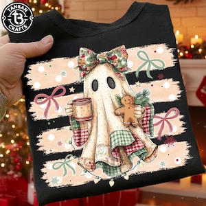May include: A black sweatshirt featuring a graphic of a ghost wearing a floral bow, holding a mug and a gingerbread cookie. The design includes horizontal brushstroke stripes in light peach, green bows, and a string of Christmas lights.