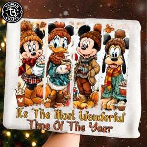 May include: A white sweatshirt featuring a graphic of Minnie Mouse, Daisy Duck, Mickey Mouse, and Goofy wearing winter hats and scarves. They are holding coffee cups amidst pumpkins. The text reads, It's The Most Wonderful Time Of The Year.