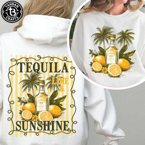 以下が含まれることがあります： テキーラボトル、レモン、ヤシの木、そして「TEQUILA LIME & SUNSHINE」の文字が黄色と黒で描かれたグラフィックデザインの白いスウェットシャツ。デザインは黄色のボーダーで縁取られています。