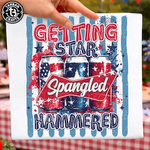 Puede incluir: Toalla cuadrada blanca con un diseño patriótico. La toalla presenta colores rojos, blancos y azules con las palabras "Getting Star Spangled Hammered" e imágenes de latas de cerveza decoradas con estrellas y rayas.