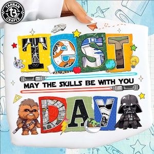 May include: White Star Wars themed graphic tee with the words "TEST DAY" in colorful letters. The design includes Darth Vader, R2-D2, Chewbacca, and Baby Yoda. The text "MAY THE SKILLS BE WITH YOU" is also included.