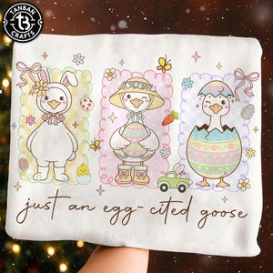 May include: White fabric featuring three cartoon geese dressed for Easter. One is in a bunny costume, another holds an egg, and the third is hatching. The text "just an egg-cited goose" is written below the illustrations.