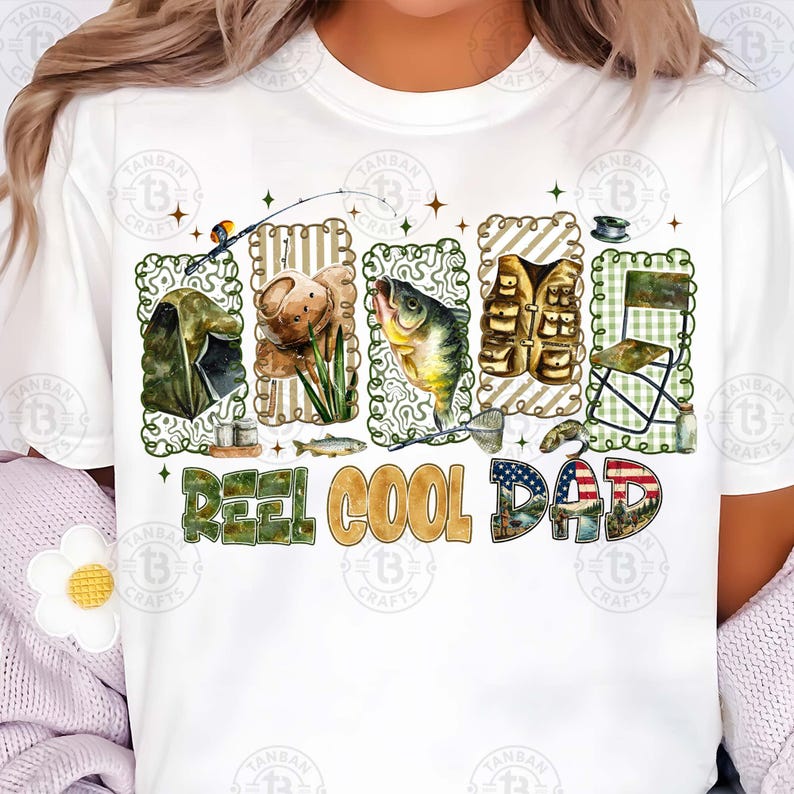 Op de afbeelding: Wit T-shirt met een visserij-thema ontwerp. Het ontwerp bevat illustraties van visgerei, een vis en de tekst "REEL COOL DAD". De letters zijn gevuld met patronen en kleuren, waaronder de Amerikaanse vlag.