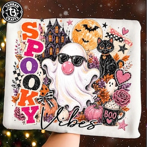 May include: A white sweatshirt featuring a graphic print with the text SPOOKY VIBES, a ghost wearing sunglasses and blowing a bubble, a black cat, a haunted house, a full moon with bats, pumpkins, a mug labeled BOO, and various floral elements.