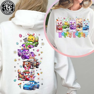 May include: White hoodie featuring a colorful Easter-themed design. The design includes cartoon cars with bunny ears, Easter eggs, and the text "Happy Easter." The cars are in various colors, including green, purple, red, and blue. The hoodie has a drawstring hood.