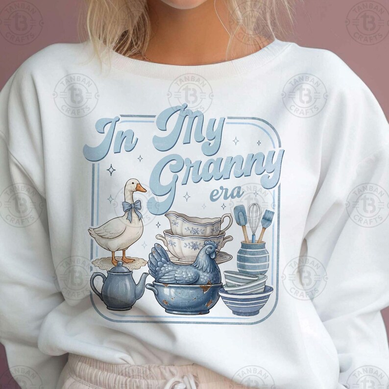 May include: White sweatshirt with a light blue graphic that reads "In My Granny era." The graphic includes a goose with a bow, a teapot, a chicken in a bowl, and stacks of bowls and dishes.