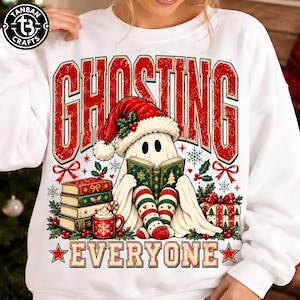 May include: A white sweatshirt featuring a graphic of a ghost wearing a Santa hat and reading a book. The text reads GHOSTING EVERYONE. The design includes a stack of books, a mug, a gift box, holly, and snowflakes in red, green, and white colors.
