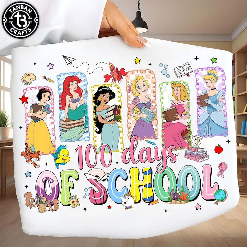 May include: A white decorative pillow featuring six Disney princesses, each holding books, with the text "100 days OF SCHOOL" in colorful letters. The design includes stars, a paper airplane, and other cartoon elements.