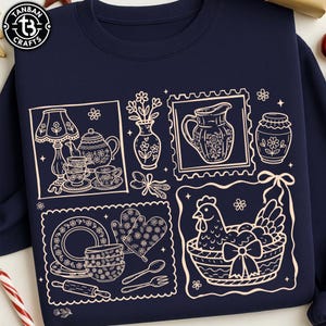 Puede incluir: Sudadera azul marino con una ilustración crema de sellos con temática de cocina. Los sellos representan una tetera, flores, una jarra, un tarro, platos, un rodillo, una gallina en una cesta y otros artículos de cocina.