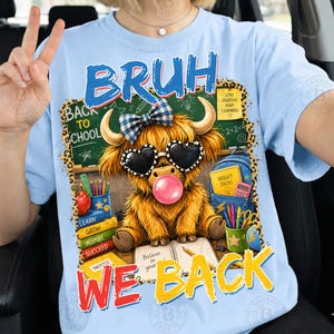 May include: A light blue t-shirt featuring a graphic of a fluffy highland cow wearing heart-shaped sunglasses and a blue plaid bow. The cow is blowing a pink bubble. The text reads BRUH WE BACK, with school supplies and a chalkboard in the background.
