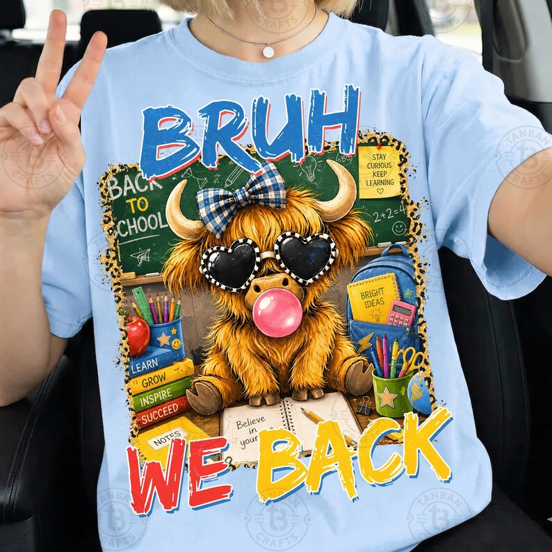 May include: A light blue t-shirt featuring a graphic of a fluffy highland cow wearing heart-shaped sunglasses and a blue plaid bow. The cow is blowing a pink bubble. The text reads BRUH WE BACK, with school supplies and a chalkboard in the background.