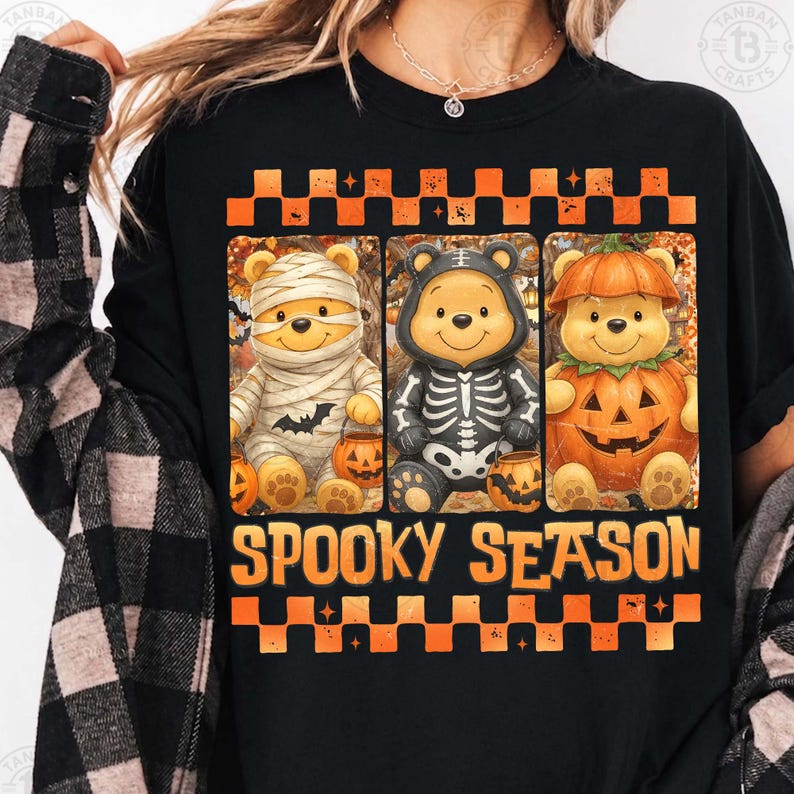May include: A black t-shirt featuring a graphic of three cartoon bears dressed for Halloween as a mummy, a skeleton, and a pumpkin. The design includes orange and black checkered borders and the text SPOOKY SEASON in orange block letters.