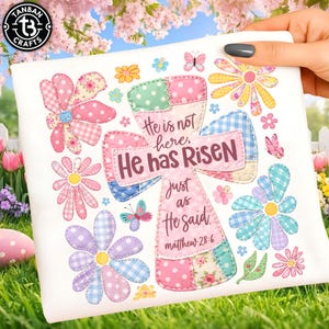 Può includere: Tessuto quadrato bianco con un disegno a croce, fiori e farfalle. La croce presenta il testo "He has Risen" e "Matthew 28:6". Il design include colori rosa, blu, verde e giallo. Il tessuto è tenuto da una mano.