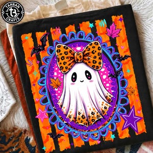 May include: A black t-shirt featuring a graphic of a white ghost with a large orange leopard print bow, centered within a blue ornate oval frame. The background includes orange and black vertical stripes, bats, maple leaves, and purple stars.