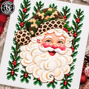 May include: A white canvas featuring a textured embroidery of Santa Claus with a thick white beard, rosy cheeks, and a hat combining camouflage and leopard print patterns, framed by vertical green pine branches with red berries and the text TANBAN CRAFTS.