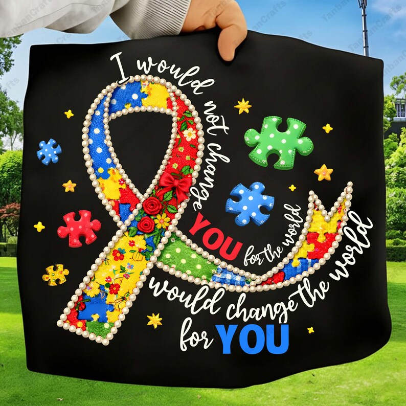 May include: Black tote bag featuring a colorful ribbon design with puzzle pieces and the text "I would not change YOU for the world, would change the world for YOU." The ribbon is decorated with flowers and pearls.