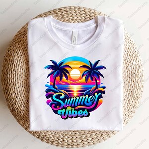 K&ouml;nnte beinhalten: Wei&szlig;es T-Shirt mit einem bunten Grafikdesign von Palmen, einem Sonnenuntergang und dem Text "Summer Vibes".