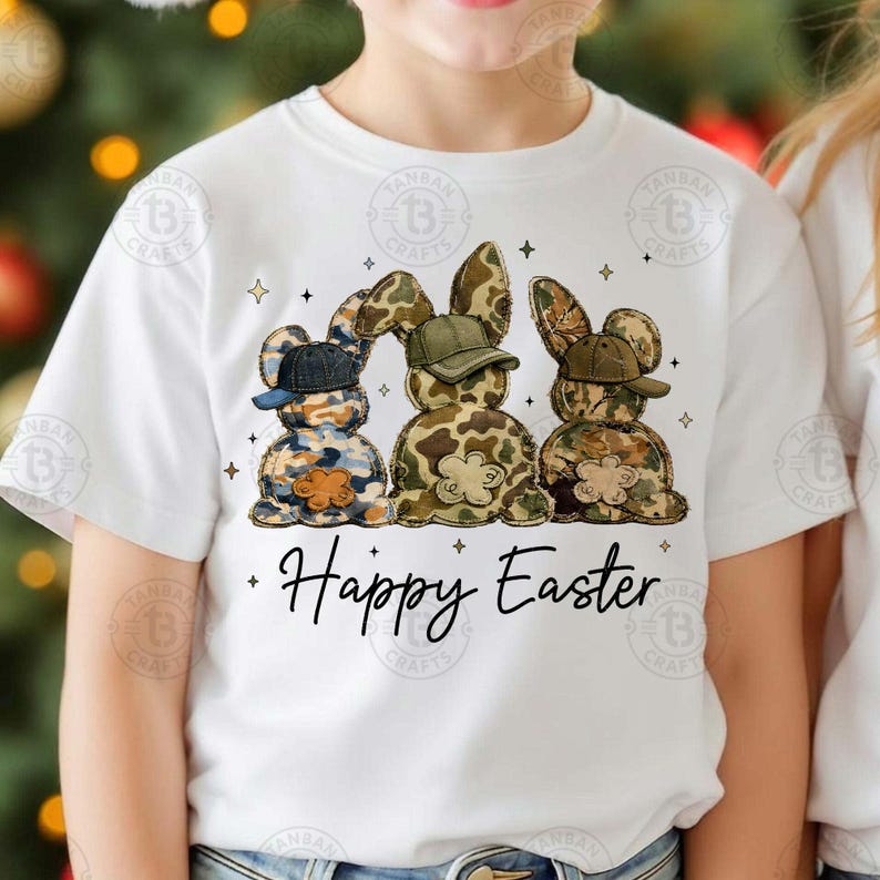 Op de afbeelding: Wit T-shirt met drie konijnenfiguren in camouflagepatronen, elk met een pet. De tekst "Happy Easter" staat eronder. Het shirt is kinderkleding, perfect voor Pasen. Het ontwerp is speels.