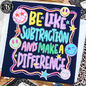 May include: A dark blue t-shirt featuring the text BE LIKE SUBTRACTION AND MAKE A DIFFERENCE in colorful, bubble-style lettering. The design is surrounded by a wavy border and includes several smiley faces with various patterns and small stars.