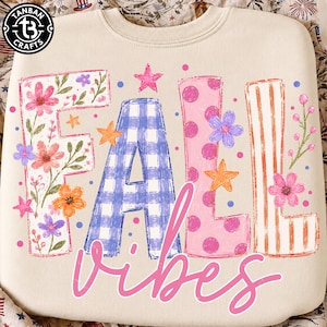 May include: A cream-colored crewneck sweatshirt featuring the word FALL in large, decorative letters. The F is floral, the A is blue gingham, the L is pink with polka dots, and the L is orange-striped. The word vibes is written in pink script.