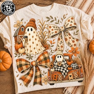 Puede incluir: Una camiseta color crema con un estampado gráfico de dos fantasmas, uno con gorro y una taza de café cerca de un granero y calabazas, y el otro sentado en la parte trasera de un camión naranja con una manta, decorado con grandes lazos.