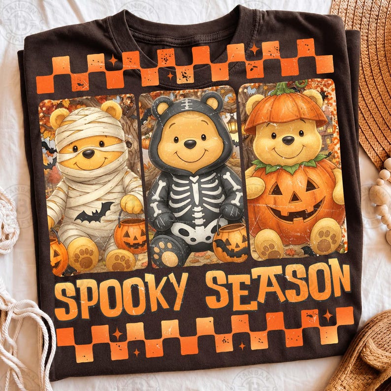 May include: A dark brown t-shirt featuring three cartoon bears in Halloween costumes: a mummy, a skeleton, and a pumpkin. The graphic includes orange and brown checkered borders at the top and bottom, with the text SPOOKY SEASON in orange letters.