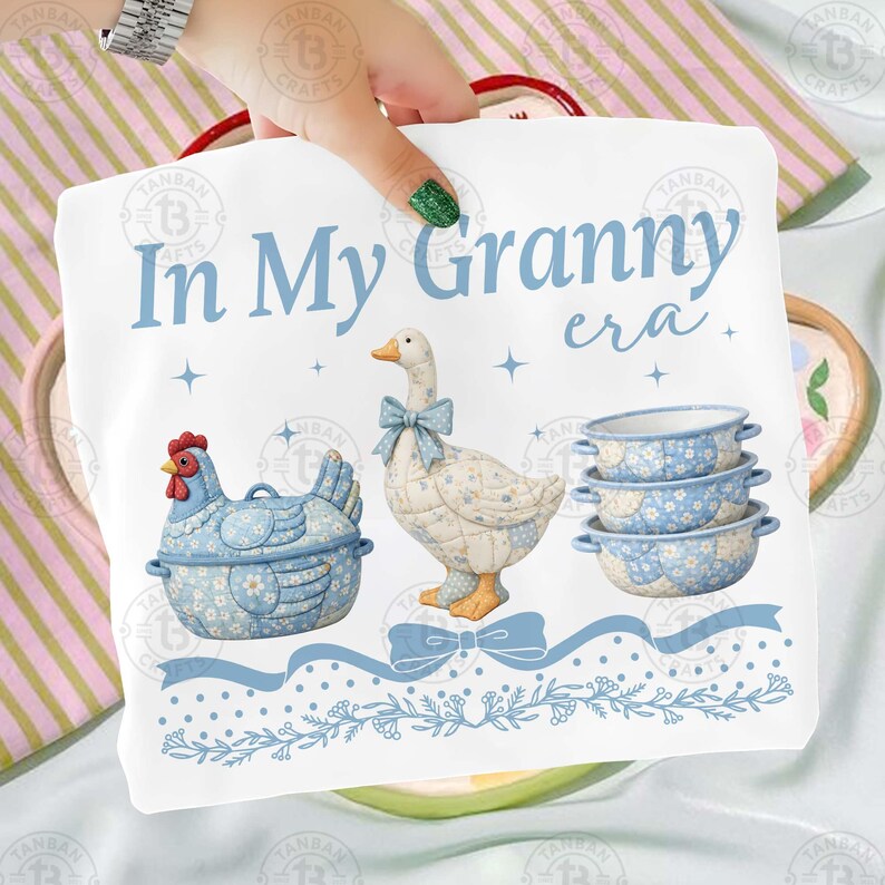 May include: A white decorative kitchen towel with the text "In My Granny era" in light blue. The towel features illustrations of a blue hen, a goose with a blue bow, and three blue bowls.