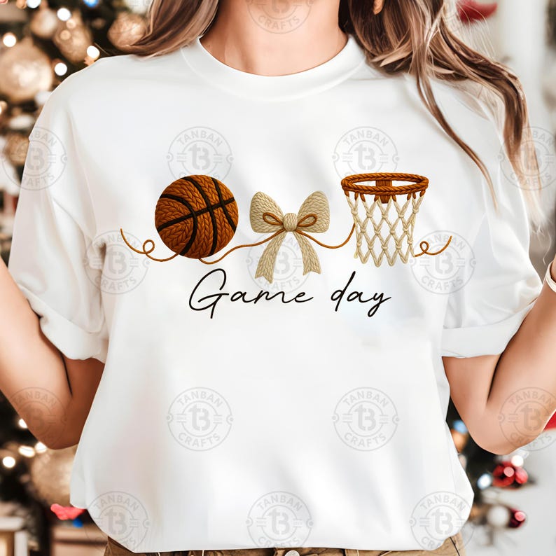 May include: White t-shirt featuring a basketball, a bow, and a basketball hoop graphic. The words "Game day" are written in a script font below the graphics. The basketball is brown with black lines.