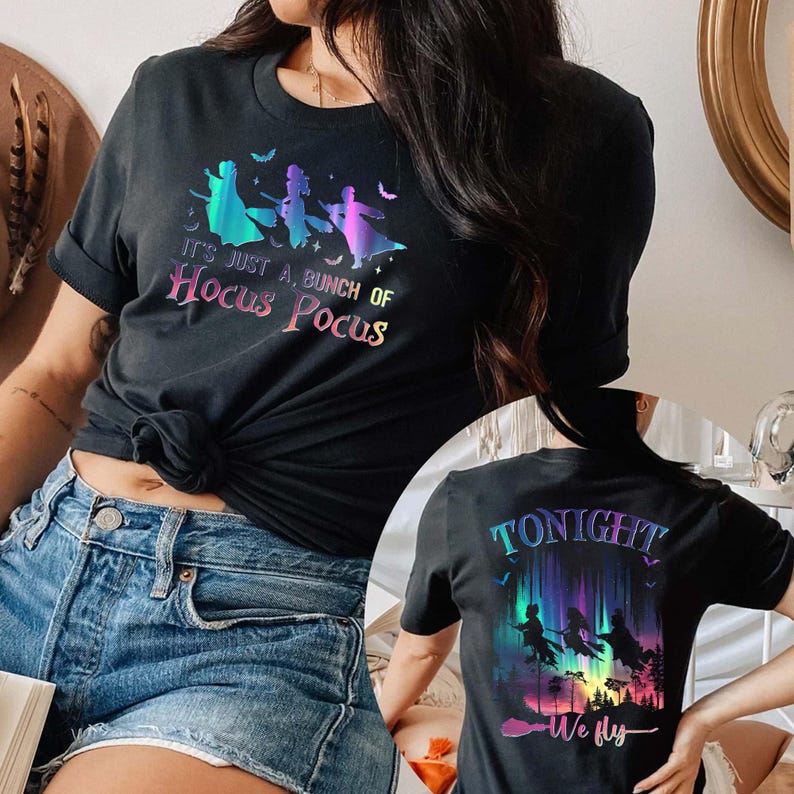 Puede incluir: Camiseta negra con la frase "It's just a bunch of Hocus Pocus" y un gr&aacute;fico de tres brujas volando en escobas. La parte trasera de la camiseta tiene el texto "Tonight We Fly" con un gr&aacute;fico similar.