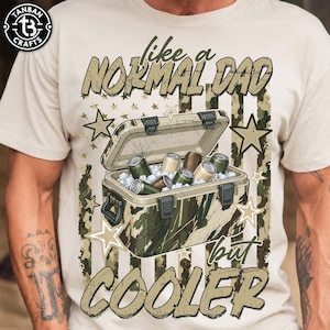 May include: Beige t-shirt with a camouflage cooler graphic filled with cans and ice. The text reads "like a NORMAL DAD but COOLER" in a distressed font. The design includes star accents.