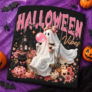 May include: A black t-shirt featuring a graphic of a white ghost on a swing, wearing a pink bow, holding a pink bubble and a coffee cup. The text reads HALLOWEEN Vibes in pink. Includes a black cat, pumpkins, flowers, and a haunted house.