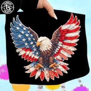 May include: Black tote bag featuring a detailed eagle design with outstretched wings. The eagle's wings are adorned with a patchwork pattern in red, white, and blue, resembling the American flag. The eagle has a white head, brown body, and yellow beak and talons. The bag has the text "TANBAN CRAFTS" in a circle.