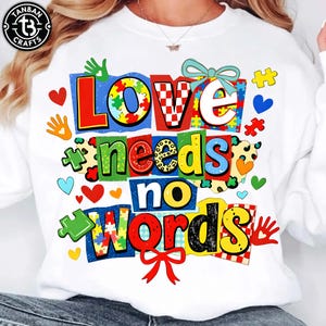 May include: White sweatshirt with the text "LOVE needs no WORDS" in colorful block letters. The design includes puzzle pieces, hearts, and handprints. A bow is at the top and bottom of the text.