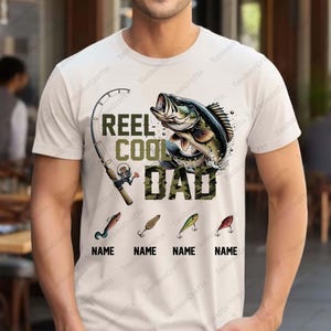 Pu&ograve; includere: T-shirt bianca a tema pesca. La maglietta presenta la scritta "REEL COOL DAD" in verde e mimetico, una grafica di un pesce, una canna da pesca e quattro esche da pesca con la parola "NAME" sotto.