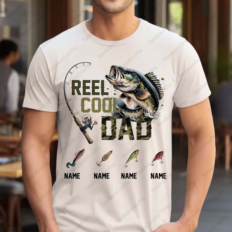 Pu&ograve; includere: T-shirt bianca a tema pesca. La maglietta presenta la scritta "REEL COOL DAD" in verde e mimetico, una grafica di un pesce, una canna da pesca e quattro esche da pesca con la parola "NAME" sotto.