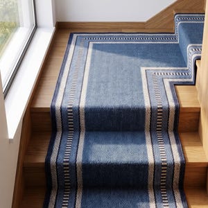 May include: A blue stair runner with a herringbone weave pattern and a border featuring cream and dark blue stripes. The runner covers the wooden steps, extending from the bottom landing up to the turn in the staircase, creating a continuous runner.
