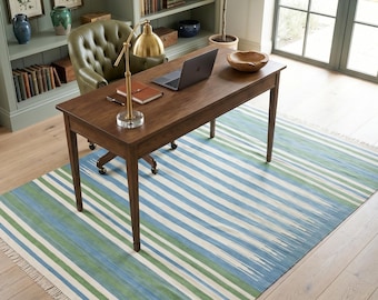 May include: A rectangular area rug featuring a pattern of horizontal stripes in shades of blue, green, and white. The rug has a flat-woven texture and includes short, off-white fringe detailing along the two shorter edges of the textile.