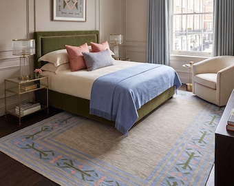 May include: A bedroom featuring an olive green upholstered bed with white bedding, pink and blue throw pillows, and a light blue throw blanket. A large area rug with a blue, green, and pink geometric border sits on dark wood flooring.
