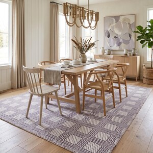 May include: A rectangular area rug featuring a repeating geometric pattern of white squares outlined in dark gray. The rug is positioned on a light-colored wooden floor beneath a wooden dining table, several wooden chairs, and a linear light fixture.