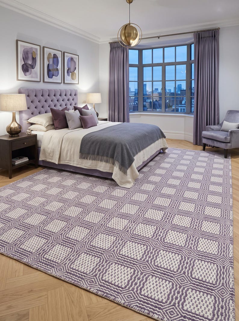 May include: A large rectangular area rug featuring a repeating geometric pattern of light purple and off-white squares. The rug has a textured, woven appearance with a grid-like design that covers the floor in a bedroom setting.