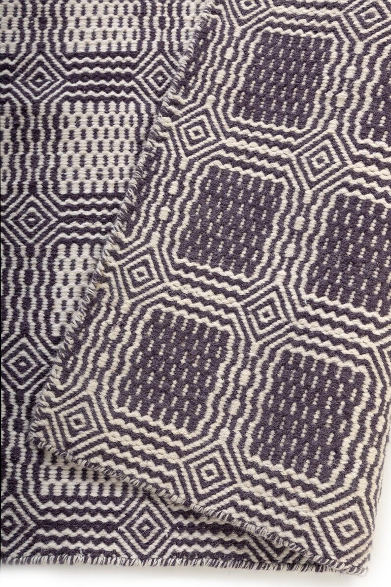 May include: A woven textile featuring a repeating geometric pattern in dark charcoal gray and off-white. The design consists of interconnected octagonal shapes and small squares, creating a textured, high-contrast surface with visible fabric weave.