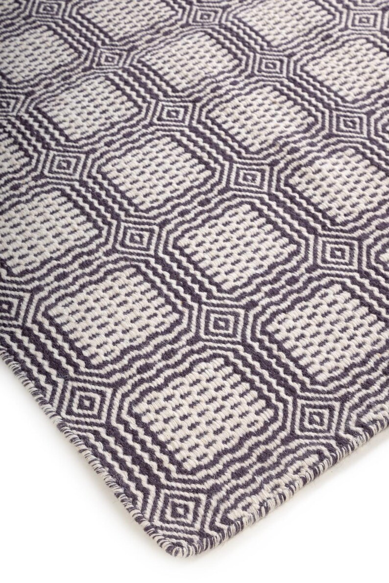 May include: A woven rug featuring a repeating geometric pattern of dark charcoal gray and off-white squares. The design consists of interconnected rounded squares with a textured, dotted interior and a thick, dark border outline throughout.